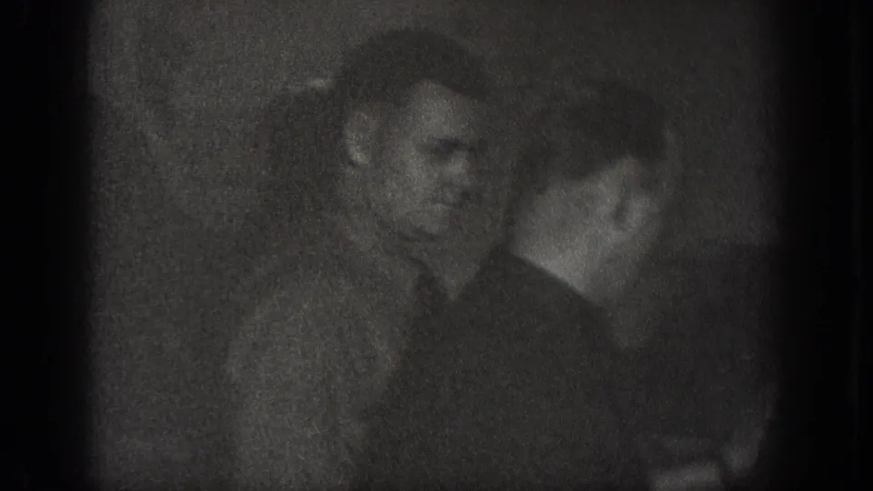 Underexposed close-up of a male figure in a dark indoor setting, Chelan, Washington, circa 1939; 8mm home movie with severe shadow detail loss.