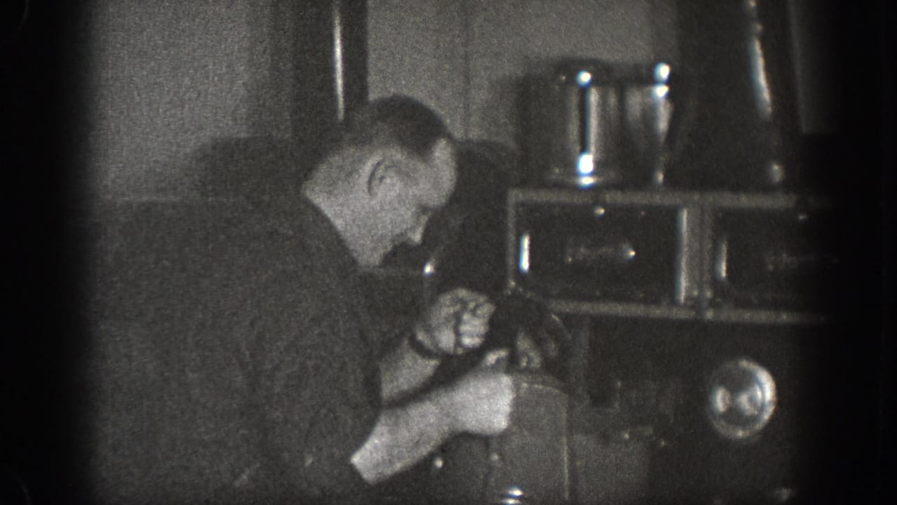 Man in a dark shirt leaning over a large boxy mechanical appliance in a dimly lit interior, with metal containers visible at upper right.