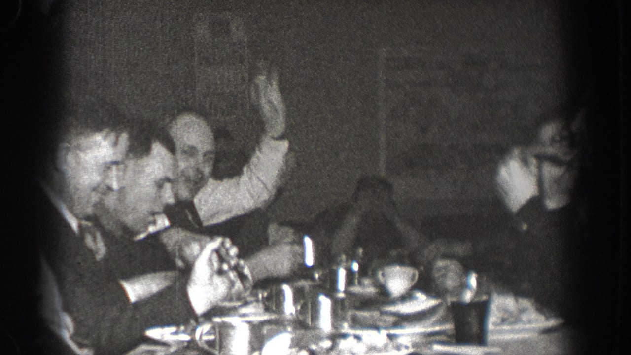 Men in suits at a communal meal in Chelan, Washington, circa 1939; one man raises a hand in an animated gesture toward others at the table.