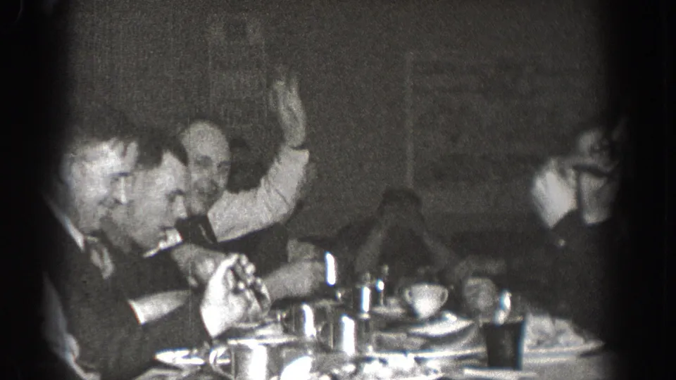 Men in suits at a communal meal in Chelan, Washington, circa 1939; one man raises a hand in an animated gesture toward others at the table.