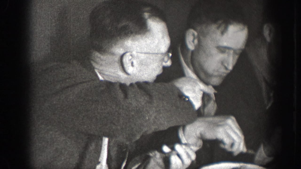 Close shot of two suited men at a dining table, one in glasses — candid 8mm home movie from Chelan, Washington, circa 1939.