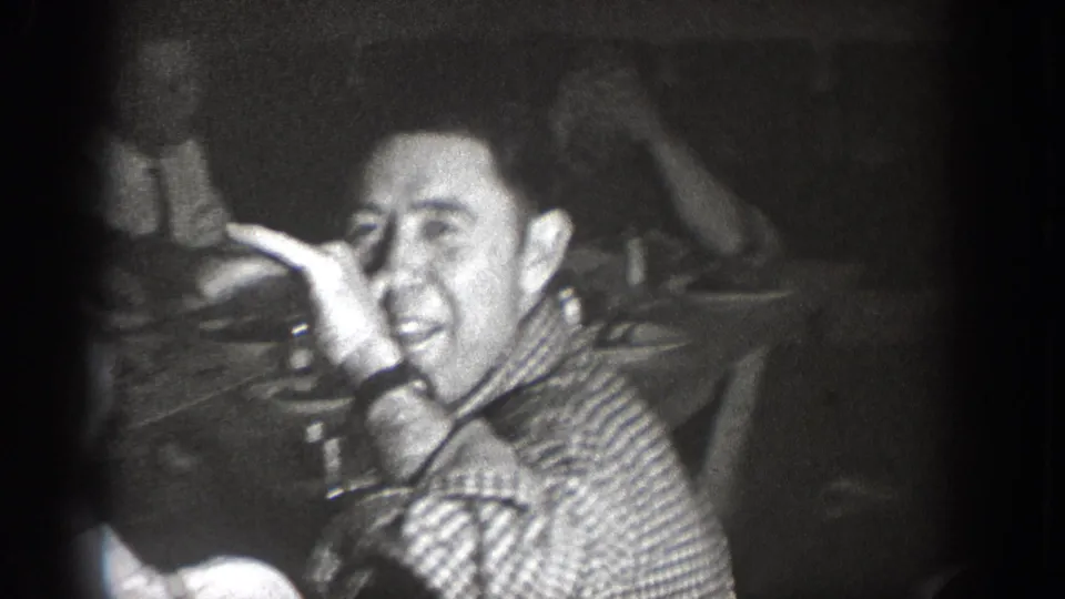 Man in a plaid checkered shirt smiling broadly at the camera and raising a hand to his face; candid home-movie moment consistent with 1930s Pacific Northwest footage.
