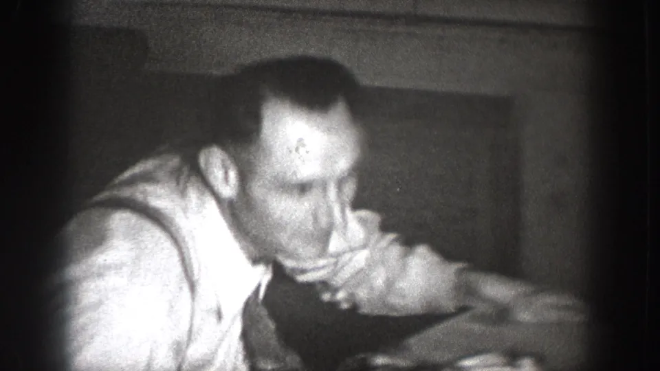 Close-up of a man in a light shirt leaning forward in a dark wood-paneled interior room, candid 8mm footage, Chelan, Washington, c.1939.