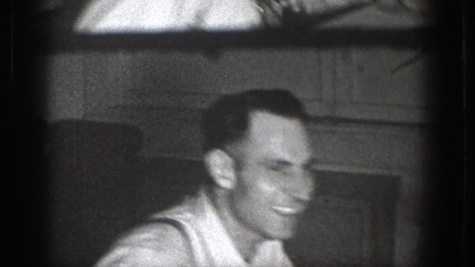 Man smiling broadly in a light undershirt, interior doorway or window frame behind him, candid 8mm footage from Chelan, Washington, c.1939.