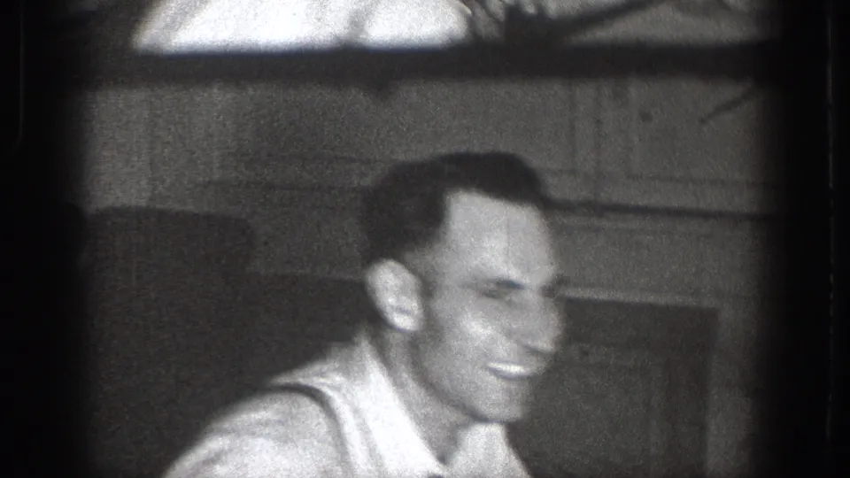 Tight close-up of a man laughing, suspenders and light undershirt visible, mantle or interior shelf behind, candid 8mm, Chelan, Washington, c.1939.