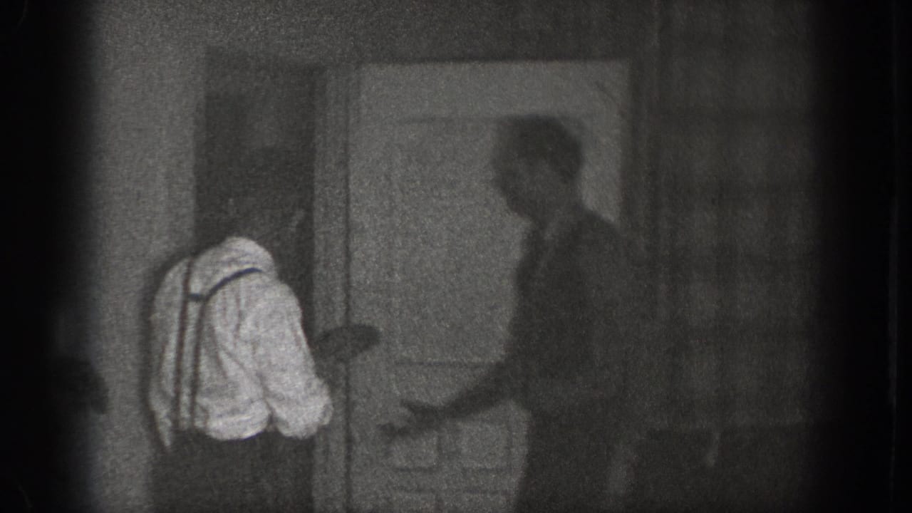 Men gather near an interior doorway as one man in suspenders leans forward.