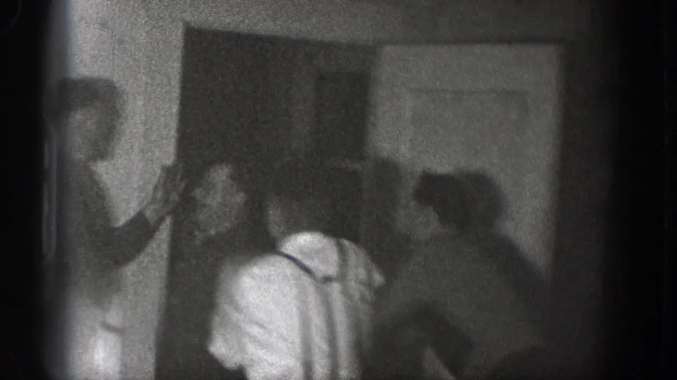 Several adult men appear clustered around a doorway in the Chelan home-movie scene, with one man in suspenders bent forward as others stand close by.