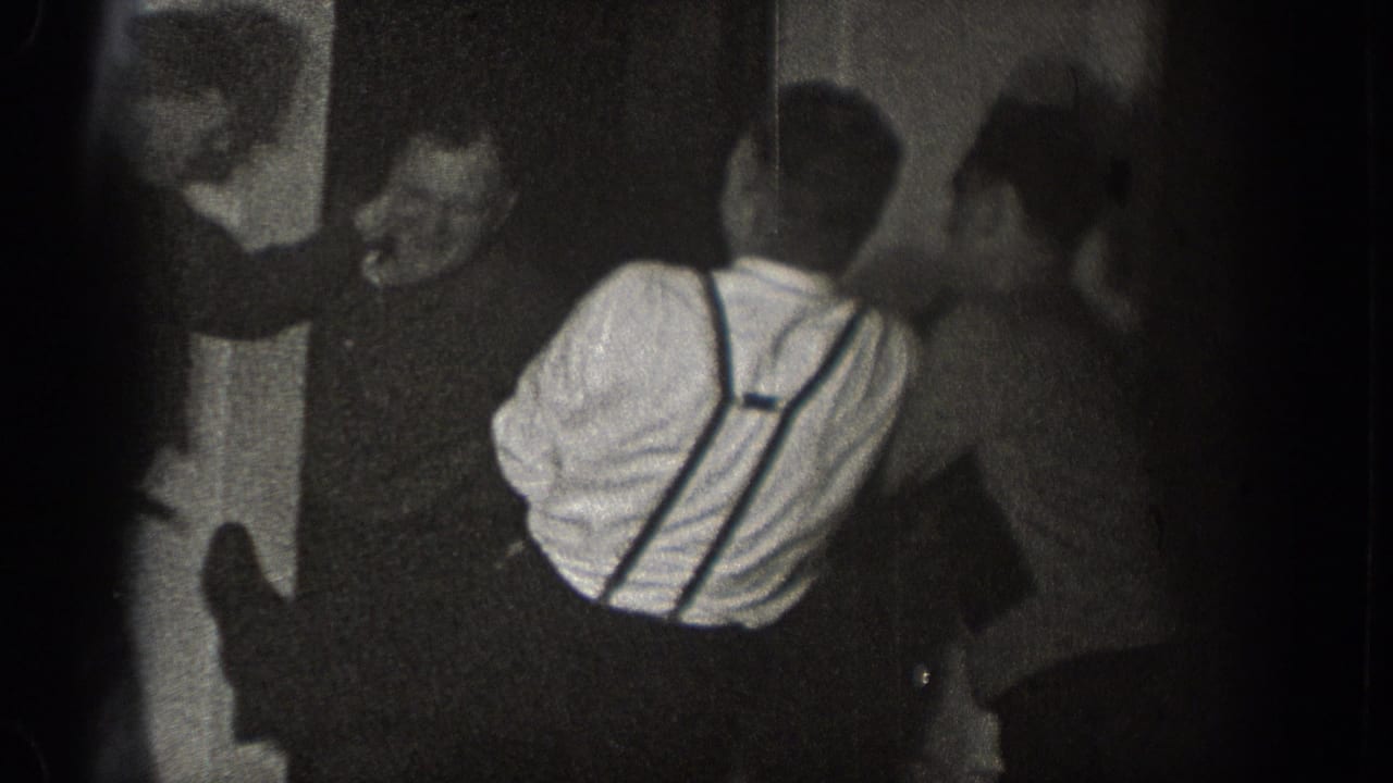 A man facing the camera appears to laugh as other adult men crowd around the man in suspenders during the 1939 Chelan indoor gathering.