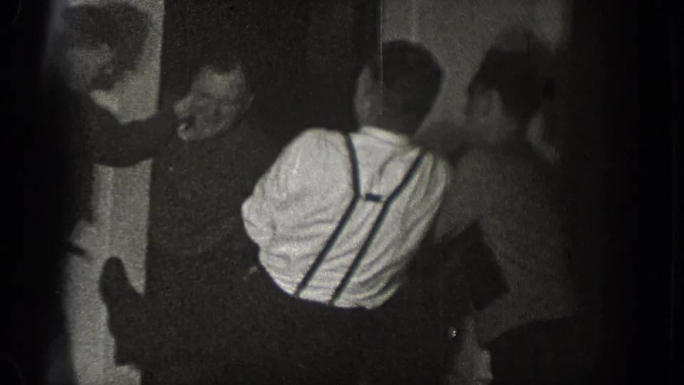 A man facing the camera appears to laugh as other adult men crowd around the man in suspenders during the 1939 Chelan indoor gathering.