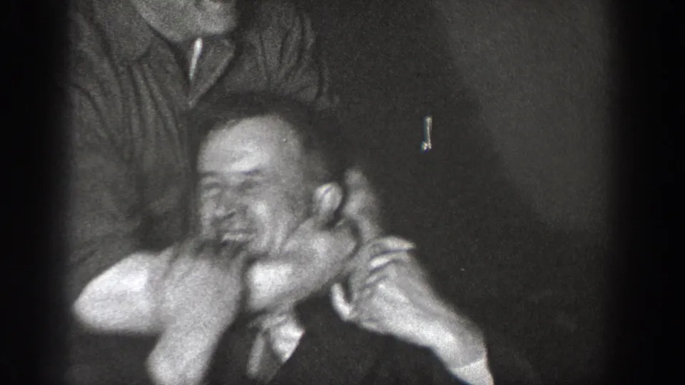 Two men in 1930s dress in a close-up playful face-grab, captured on 8mm home movie film, likely Chelan, Washington, circa 1939.