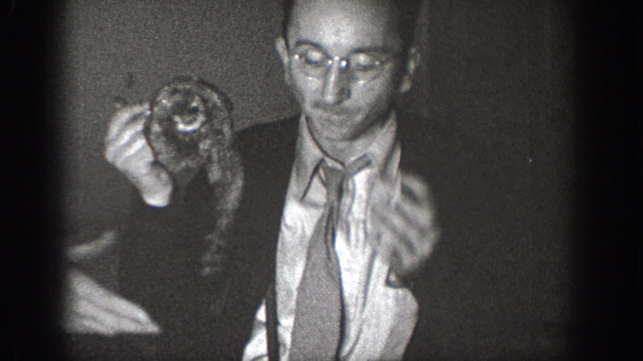 Man wearing round wire-frame glasses and a suit holds a small live animal near his face in a candid 8mm home movie, likely Chelan, Washington, circa 1939.