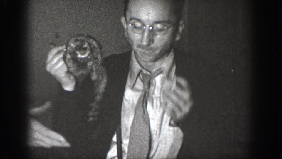 Man wearing round wire-frame glasses and a suit holds a small live animal near his face in a candid 8mm home movie, likely Chelan, Washington, circa 1939.