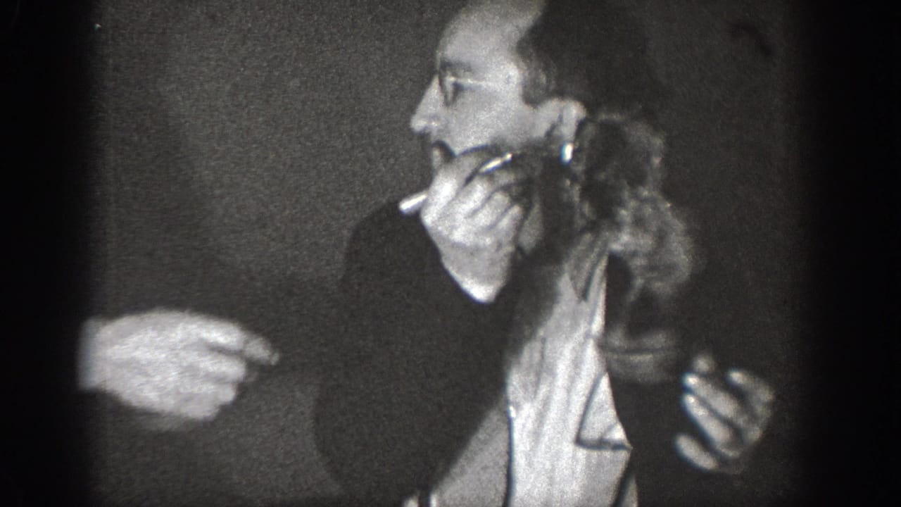 Man with a cigarette holds a small live animal as another person's hand points toward it, in 8mm home movie footage, likely Chelan, Washington, circa 1939.
