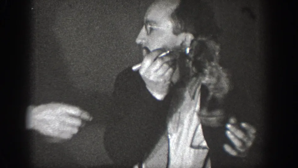 Man with a cigarette holds a small live animal as another person's hand points toward it, in 8mm home movie footage, likely Chelan, Washington, circa 1939.