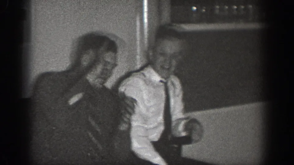 Two men in dark suits and ties laugh together in a domestic interior, Chelan, Washington, circa 1939, filmed on 8mm.