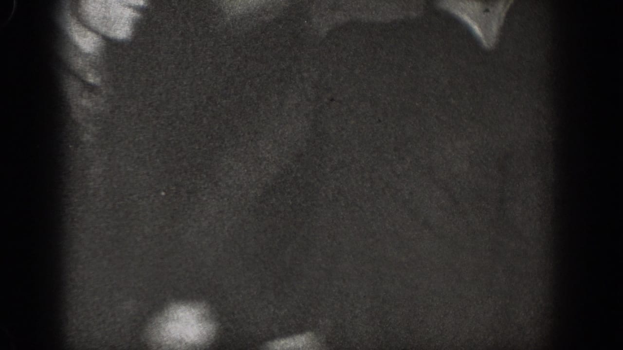 Severely underexposed 8mm frame with a partial dark figure silhouette visible at the left edge.