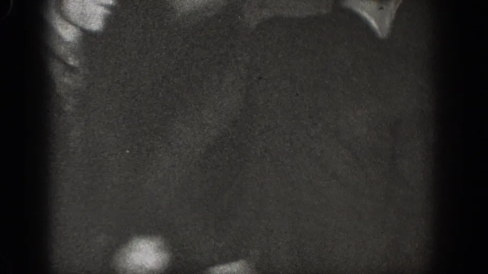 Nearly black frame from a 1930s 8mm home movie; a partial figure silhouette is barely discernible at the left edge.