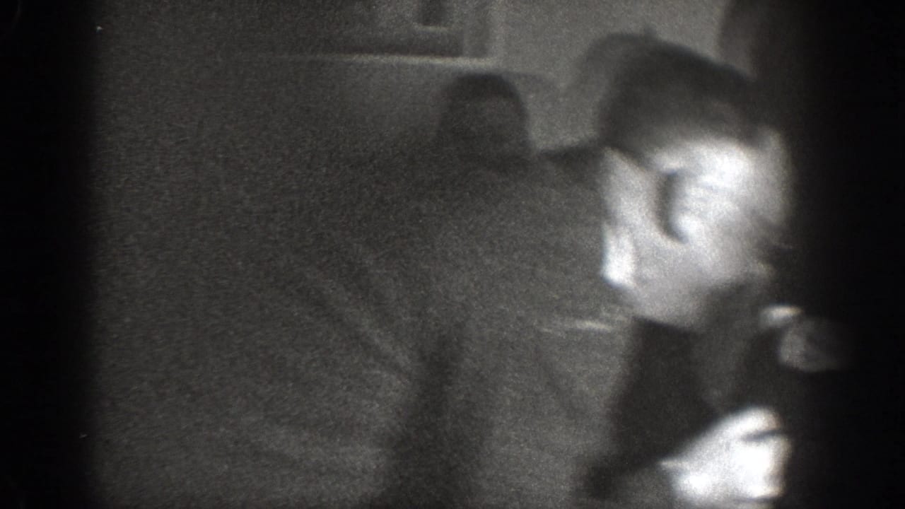 Motion-blurred frame from a 1939 8mm home movie showing a man in a dark suit in mid-movement inside a domestic interior.