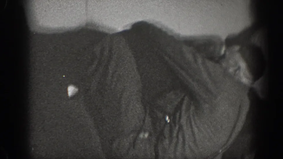 Extreme close crop on a man's torso in dark period clothing with a second figure at the frame edge; domestic interior, ca. 1939.