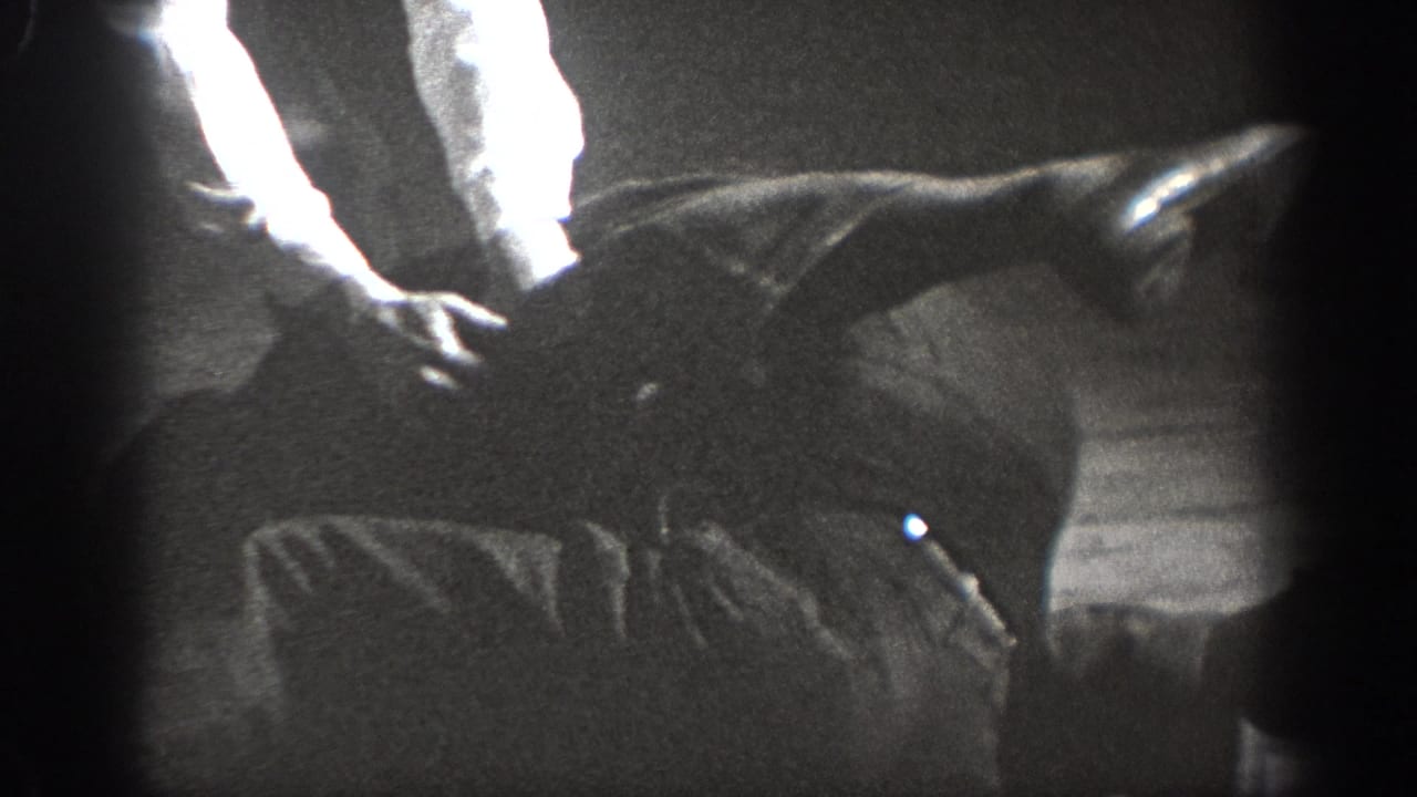 Close-up of grappling limbs and torsos on a wooden floor in black-and-white 8mm footage.