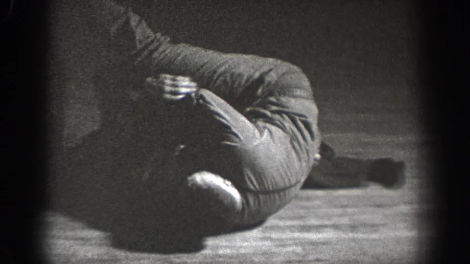 Young man crouched defensively on a wooden floor in dark clothing, Chelan, Washington, circa 1939, 8mm home movie.