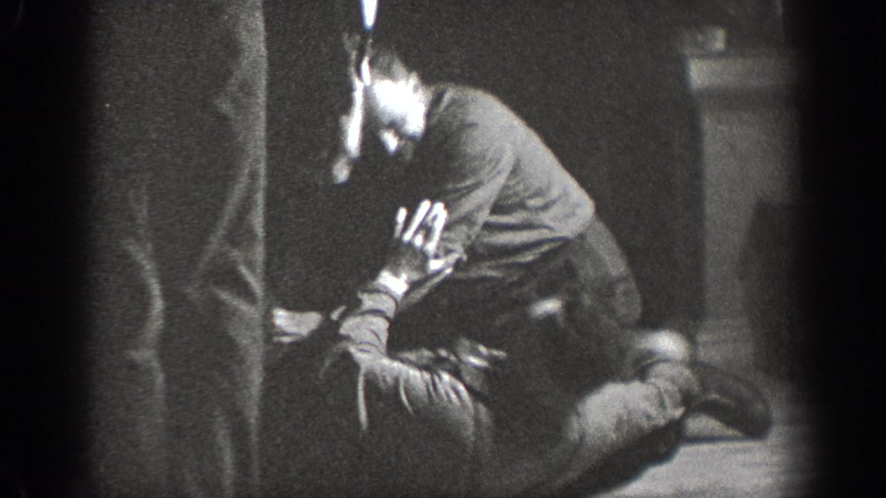 Young man crouching on an indoor wooden floor with face partially visible, background wall at right, Chelan, Washington, circa 1939.