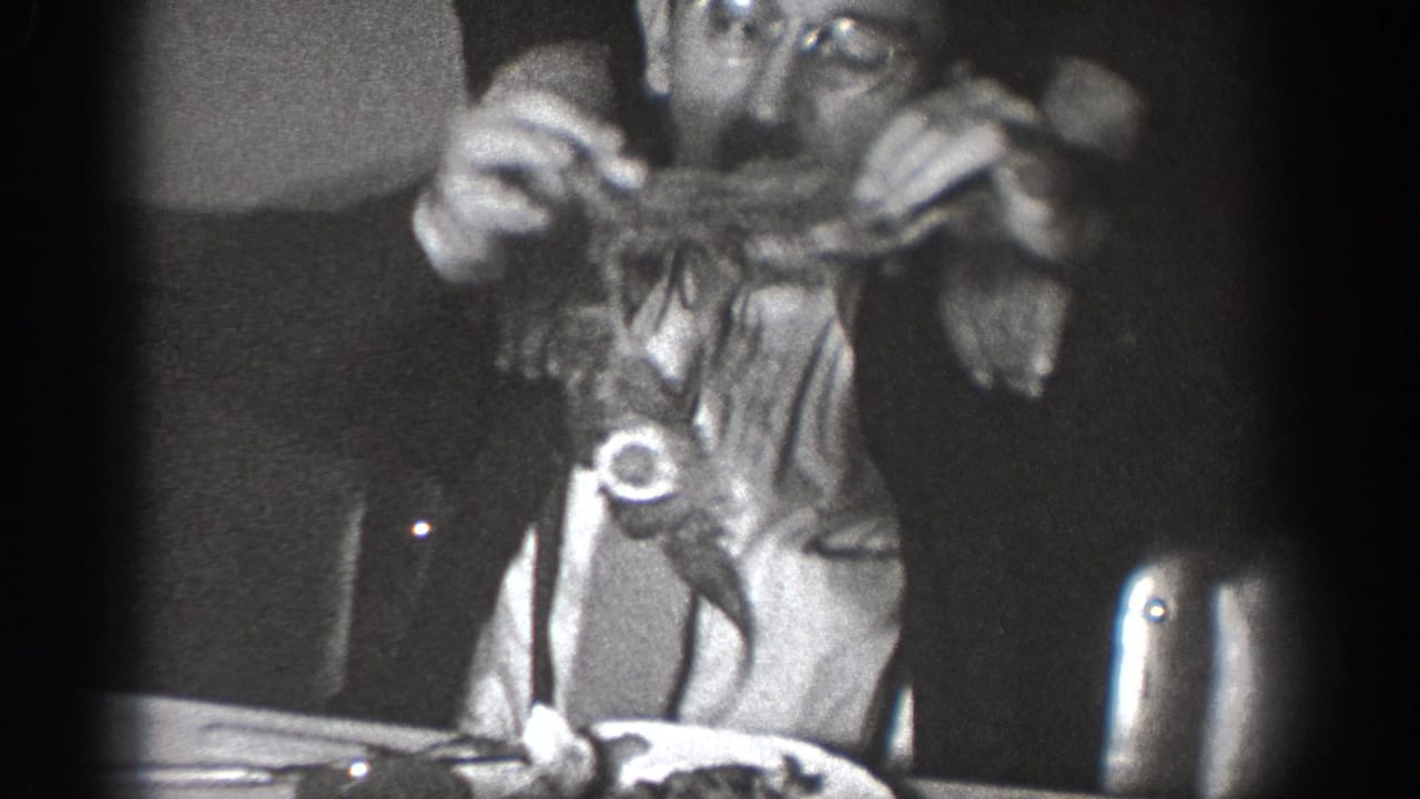 Candid 8mm frame from an apparent 1939 home movie in Chelan, Washington; adult with glasses lifts food at a dining table.