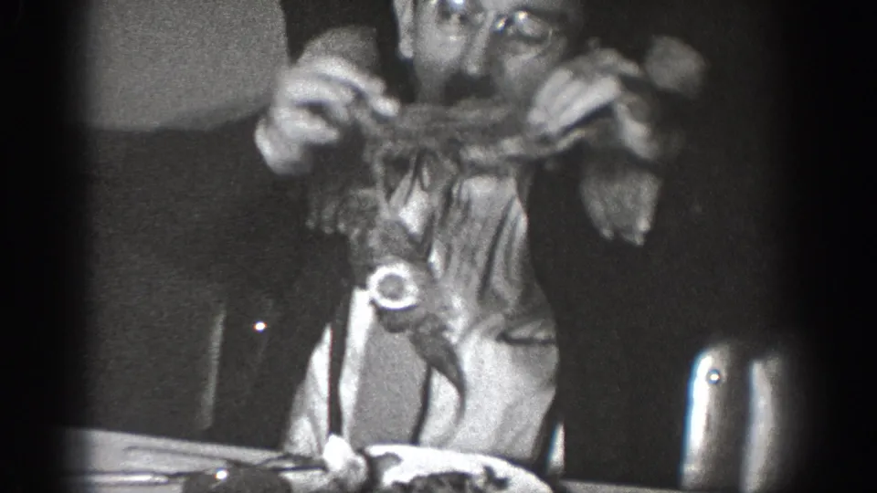 Candid 8mm frame from an apparent 1939 home movie in Chelan, Washington; adult with glasses lifts food at a dining table.