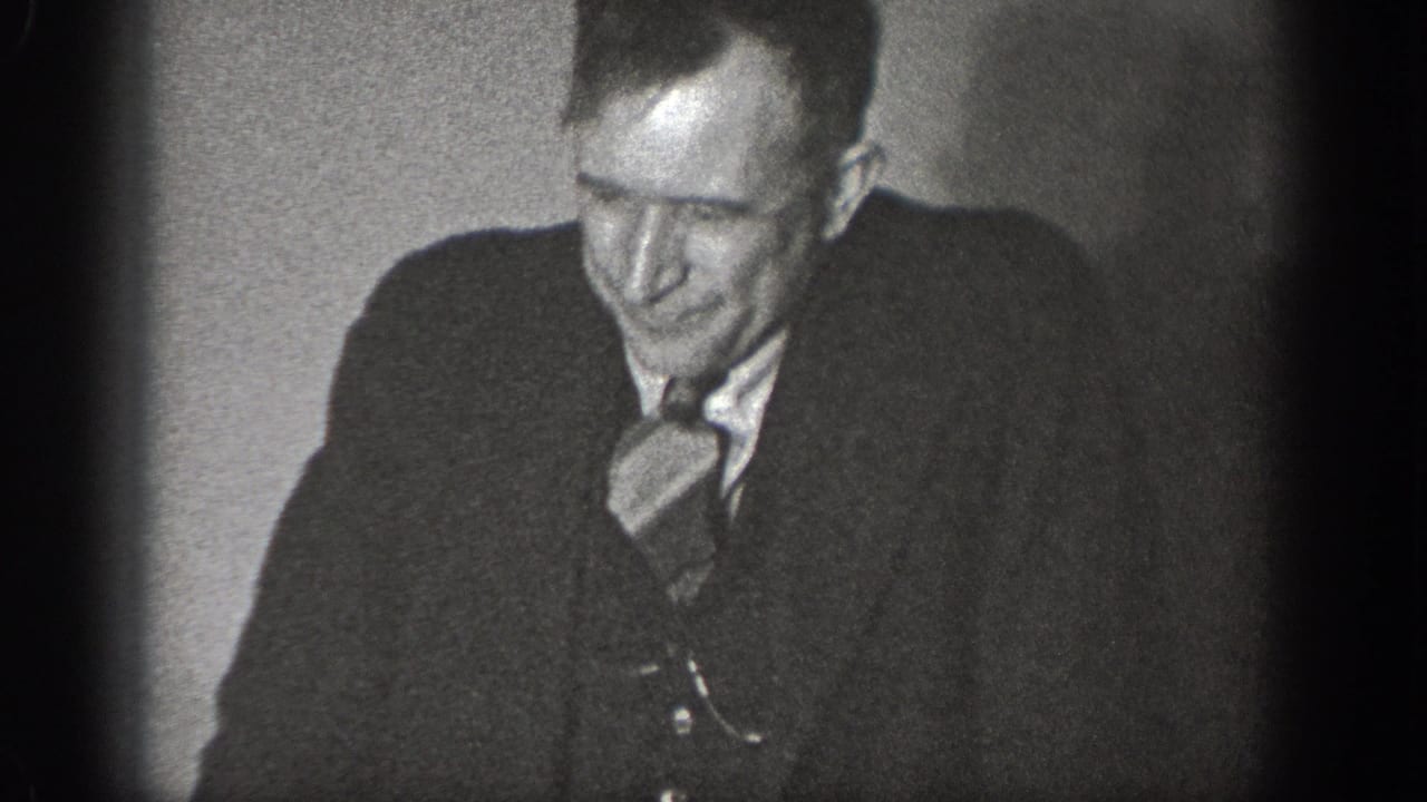 Medium close-up of a man in late-1930s suit and tie glancing down, from a 1939 home movie in Chelan, Washington.