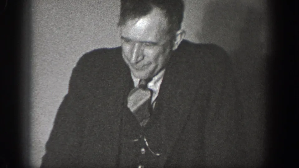 Medium close-up of a man in late-1930s suit and tie glancing down, from a 1939 home movie in Chelan, Washington.