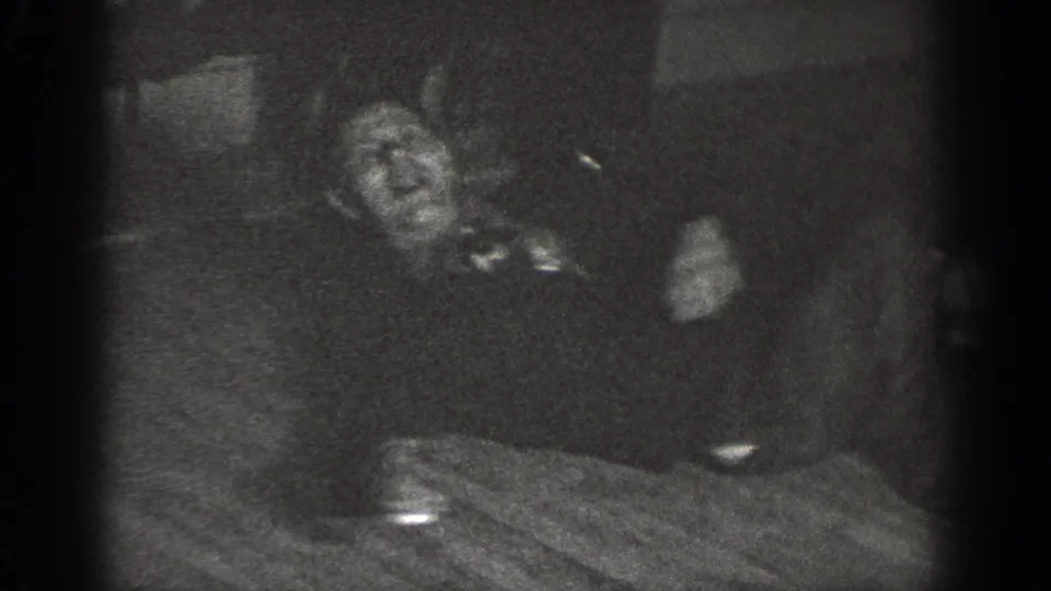 Underexposed 8mm frame showing two adults at a dining table, with motion blur and a dish or cup visible on the surface, c. 1939.
