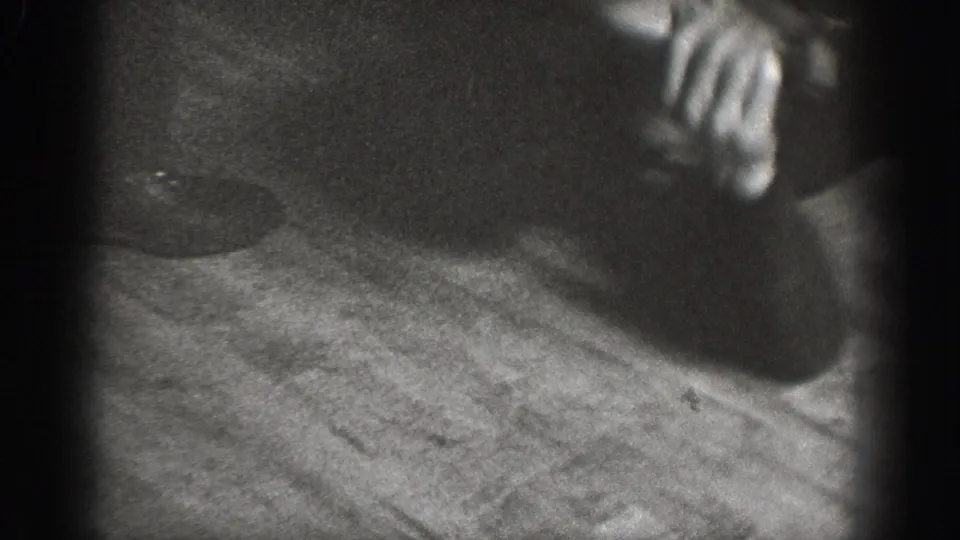 Low-angle close-up of hand reaching toward wood-plank floor; dark circular object on floor nearby; 8mm home movie footage, circa 1939.
