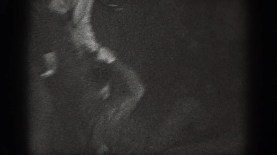 Tight close-up profile of a man in dark clothing, shot in very low light with extreme grain, from an 8mm home movie that may date to 1939.