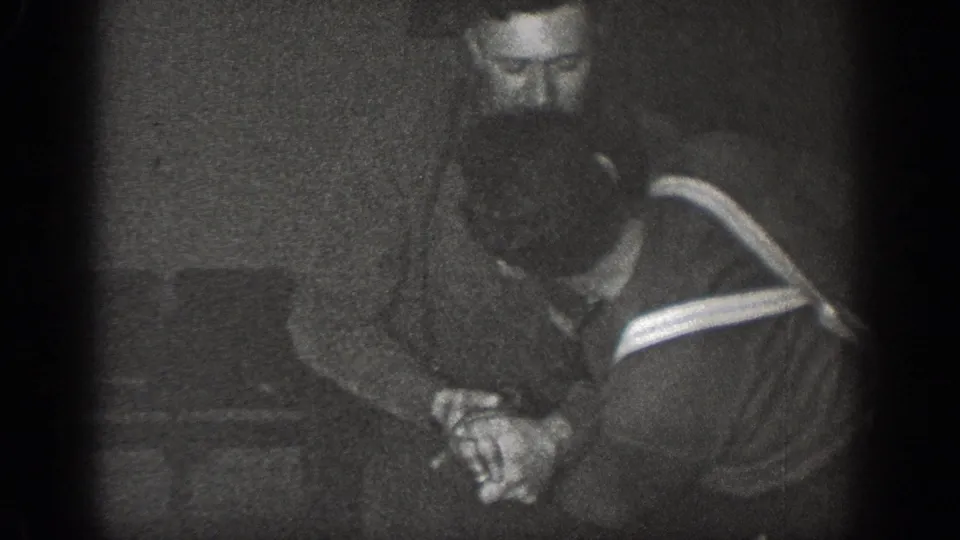 Two men standing close together in a dark interior, one wearing a diagonal-stripe sweater; 8mm home movie, Chelan, Washington, circa 1939.