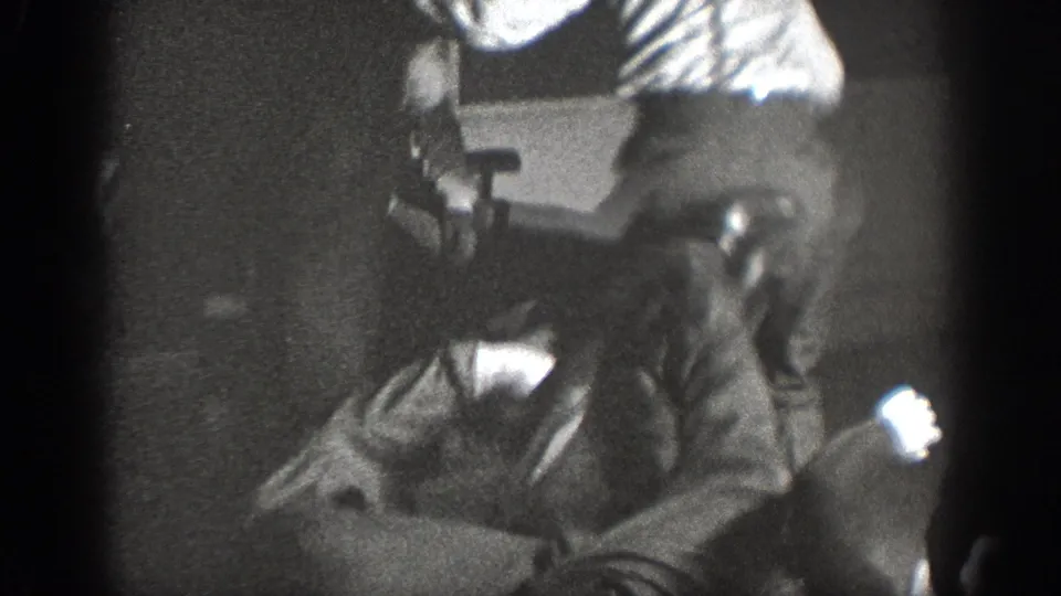 8mm home movie frame circa 1939, possibly Chelan, Washington, two men in apparent physical confrontation in a dark room with a chair and bright ambient light source visible.