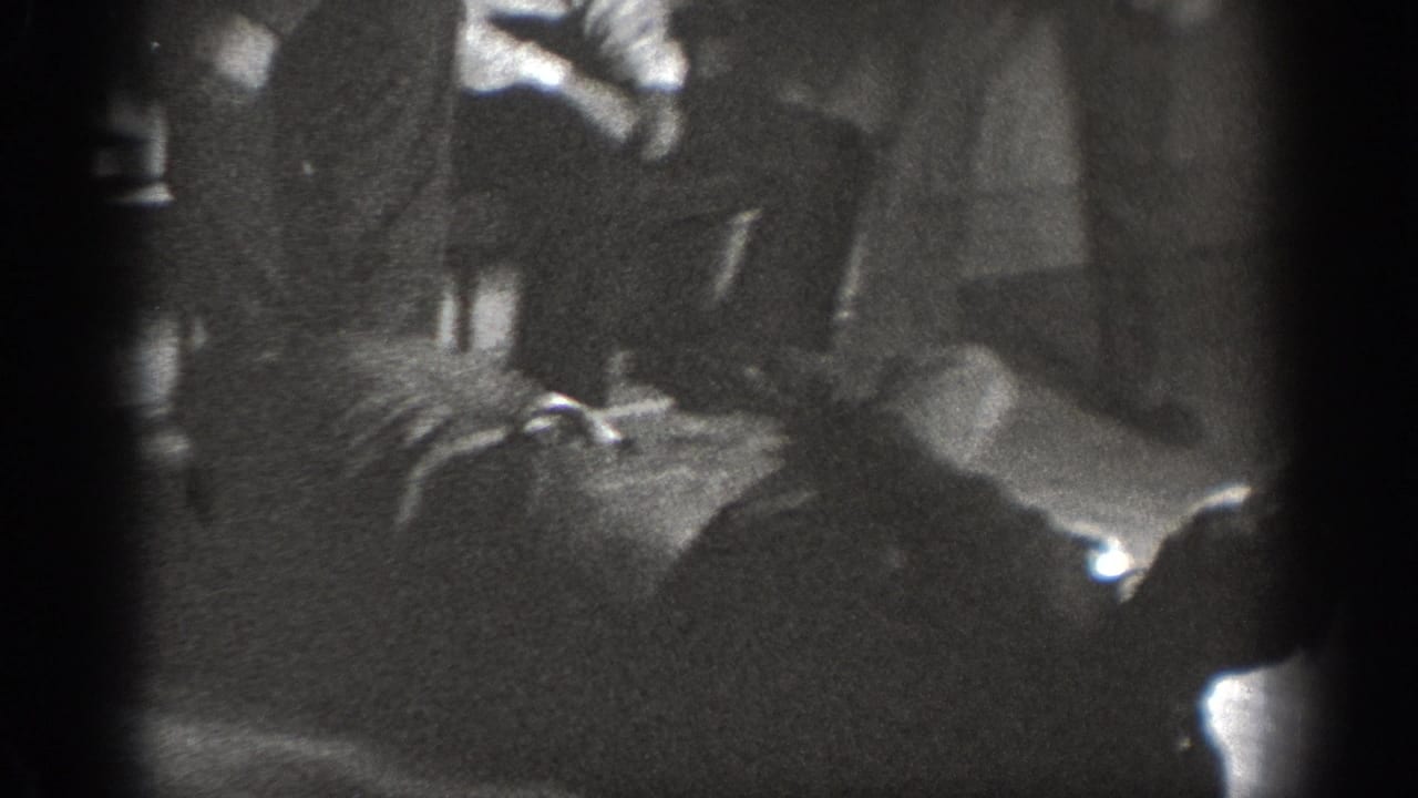 Heavily underexposed 8mm frame showing multiple men in close physical contact on a dark indoor floor.
