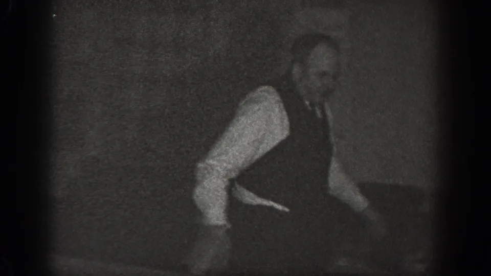 A man wearing a vest in a low crouching or active stance on a wooden floor, captured on 8mm home-movie film around 1939 in Chelan, Washington.