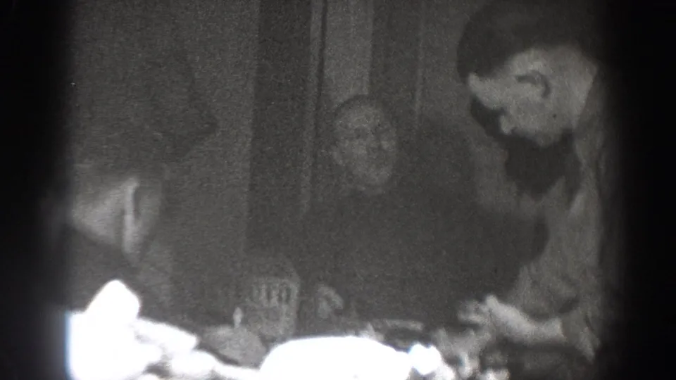 Group of men gathered around a dinner table full of dishes in a domestic setting, captured in grainy 8mm footage consistent with late 1930s home-movie style from Chelan, Washington.