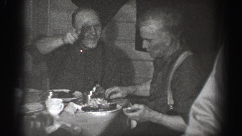 8mm home movie frame circa 1939 showing two men laughing at a domestic dinner table; the left man wears suspenders and is mid-laugh.