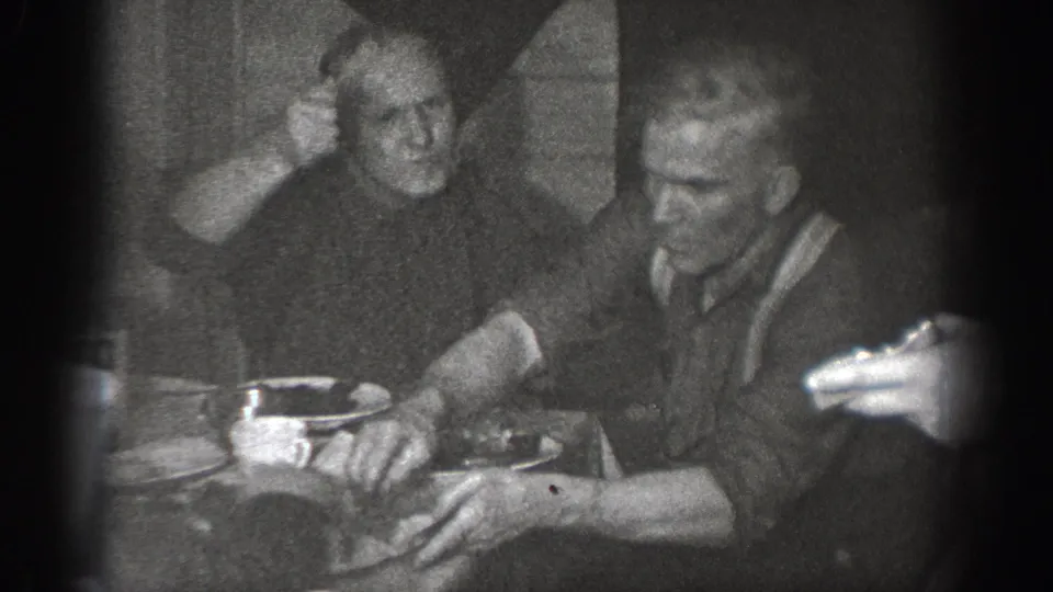 8mm home movie frame circa 1939 of two men at a domestic dinner table in Chelan, Washington; one man reaches across toward his companion.