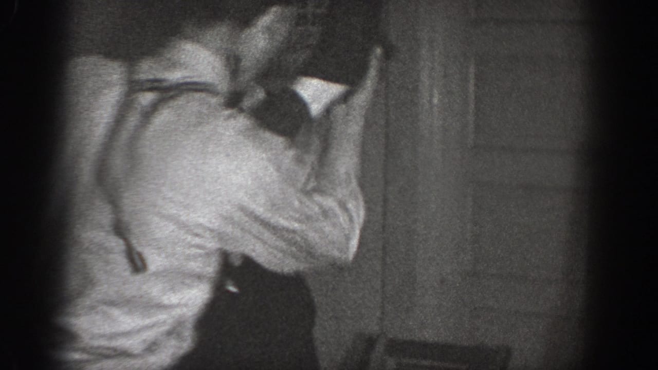 Two men roughhousing in a dim indoor setting, possibly a 1939 Chelan, Washington home; suspenders visible on one figure; 8mm film vignetting and grain throughout.