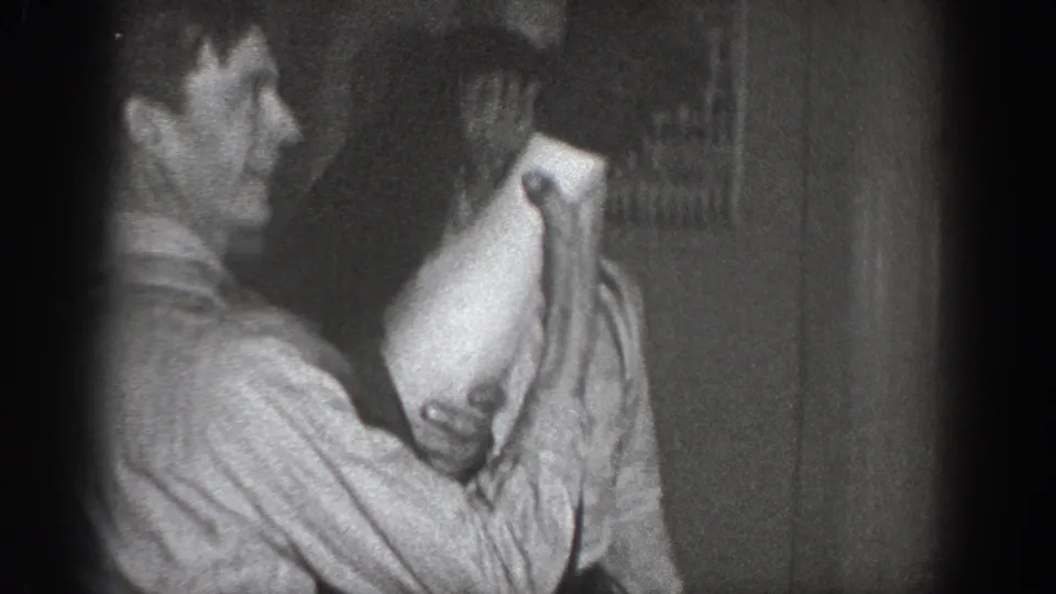 Partial profile of an adult male in a light striped shirt mid-grapple in a dim interior; an unidentified framed item visible on the wall behind, consistent with a 1930s domestic setting.
