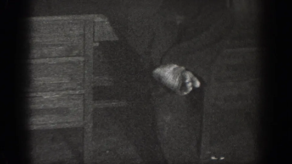 8mm home movie, ca. 1939, Chelan, Washington: man crouching or falling near wooden furniture in a dim interior, hands near the floor.