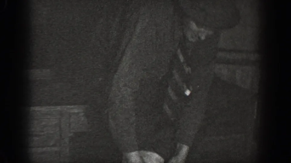 Tight 8mm close-up of a man in dark suit bending forward in what appears to be a storage room interior, Chelan, Washington, ca. 1939.