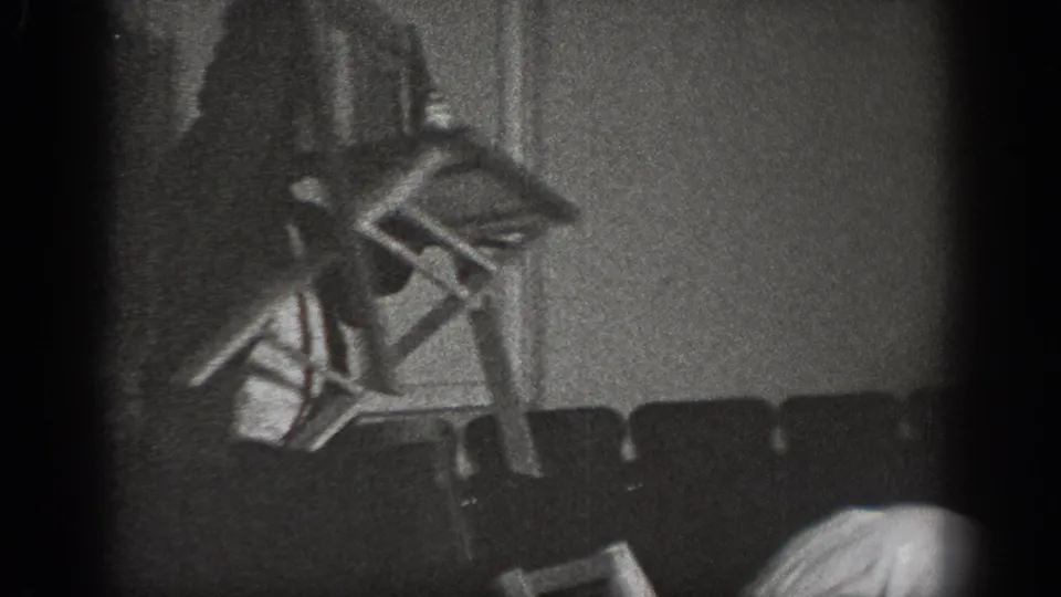 A wooden chair in motion in a darkened room with rows of empty seats visible in the background, suggesting a hall or lodge interior, circa 1939.