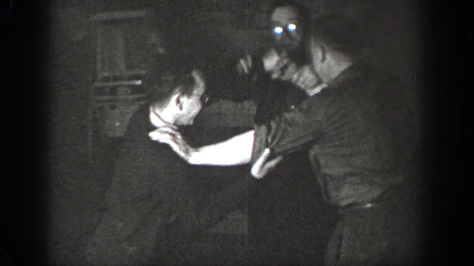 Two men in a playful mock grapple, faces illuminated by spotlight against a dark interior background, Chelan, Washington, circa 1939.