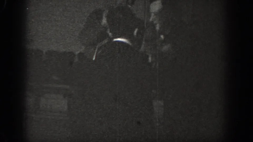 Two adult men in a playful scuffle viewed largely from behind in a dimly lit interior, from a circa-1939 8mm home movie.