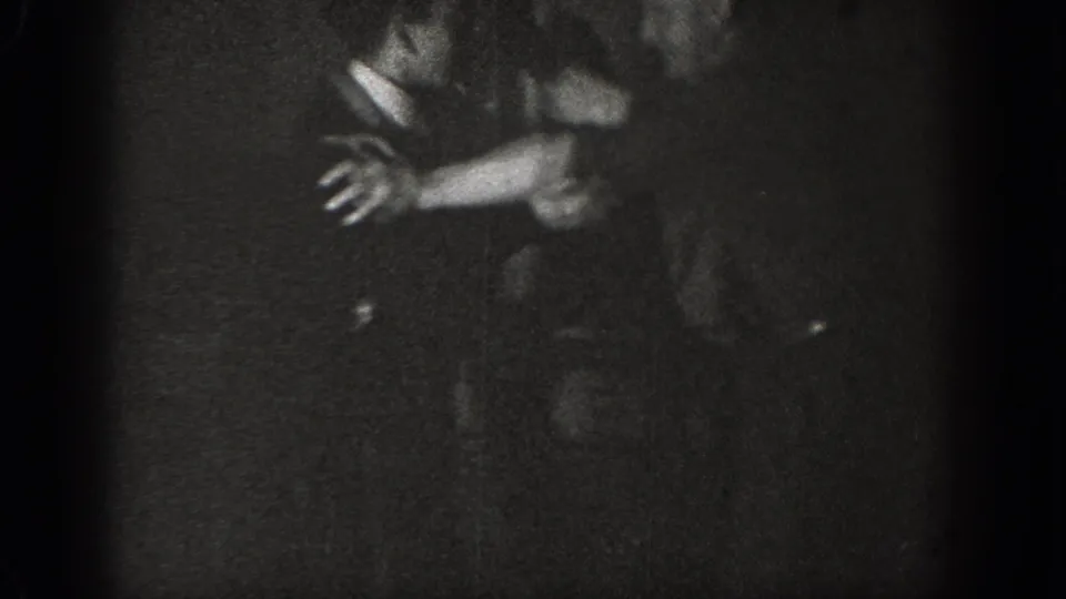 Two adult men mid-scuffle with arms extended in a heavily underexposed interior, from a circa-1939 8mm home movie.