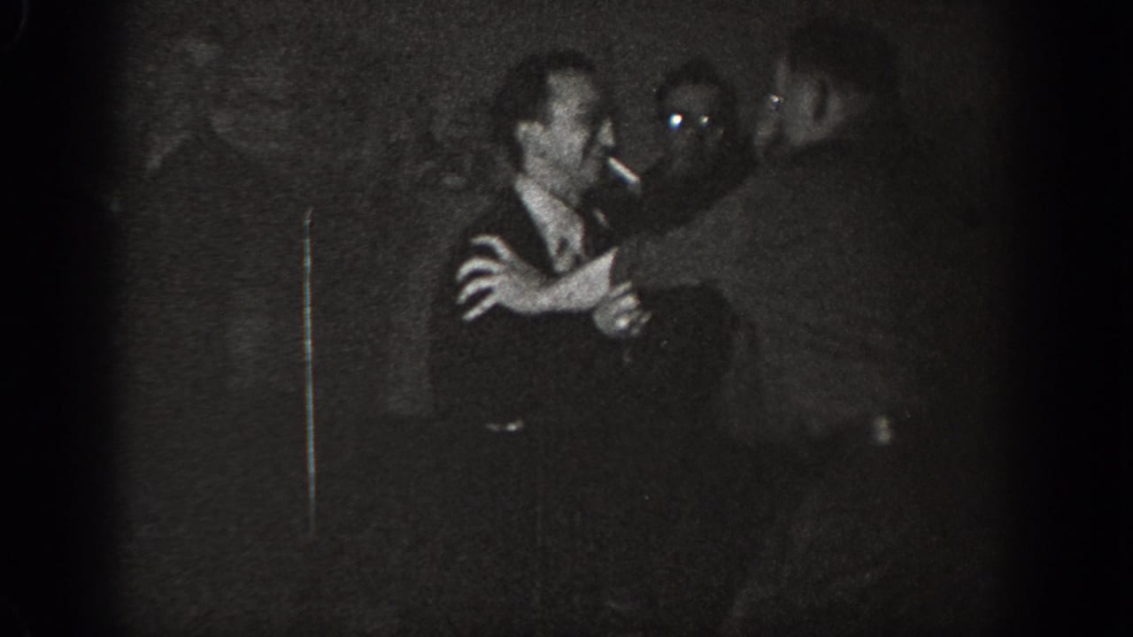 Two men grappling at close range in a dark exterior setting, possibly Chelan, Washington, circa 1939; grainy underexposed 8mm home-movie footage.