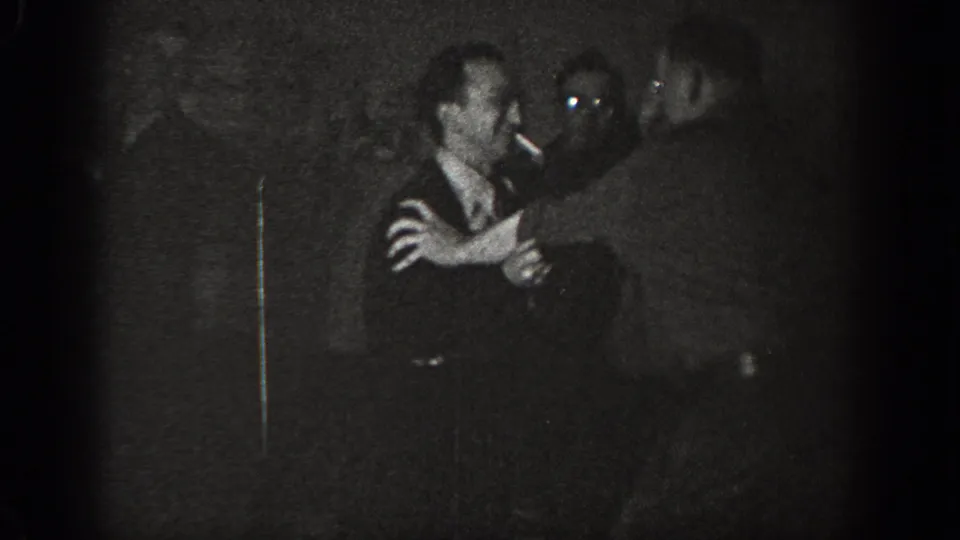 Two men grappling at close range in a dark exterior setting, possibly Chelan, Washington, circa 1939; grainy underexposed 8mm home-movie footage.